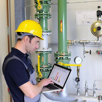 Techniker mit gelbem Helm prüft Rohre mit Laptop in der Hand